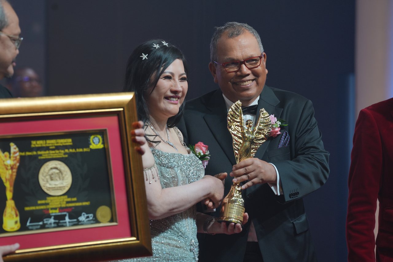 DR. SHEKINAIH SIEW SIN YAP shakes hands with Tun Md Raus Sharif as he hands her the gold trophy, her framed certificate in the foreground