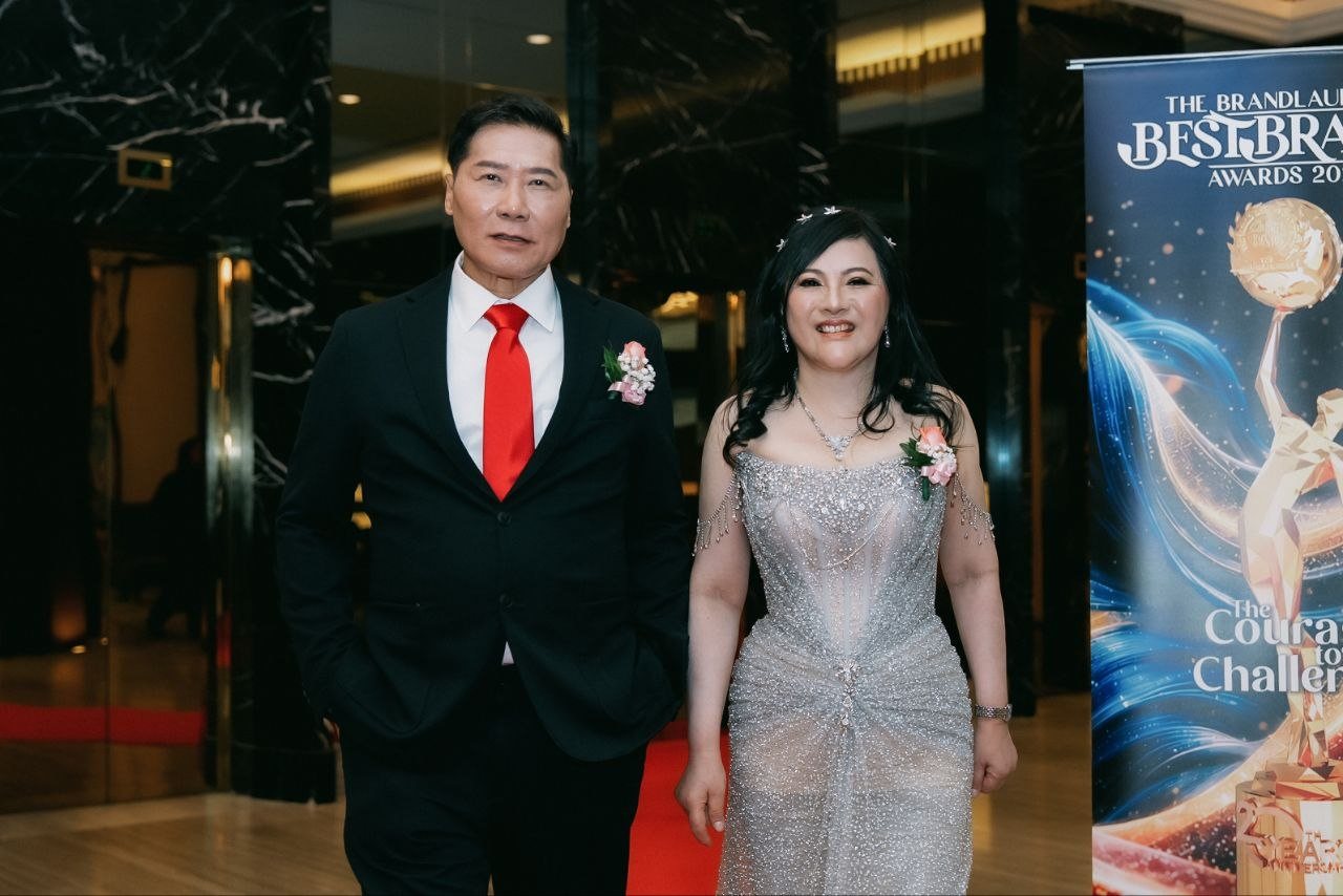 DR. SHEKINAIH SIEW SIN YAP and DR. J AARON K DAVID walk side by side along the red carpet through the marble lobby of The Majestic Hotel Kuala Lumpur, beside a banner for The BrandLaureate BestBrands Awards 2026 reading The Courage to Challenge