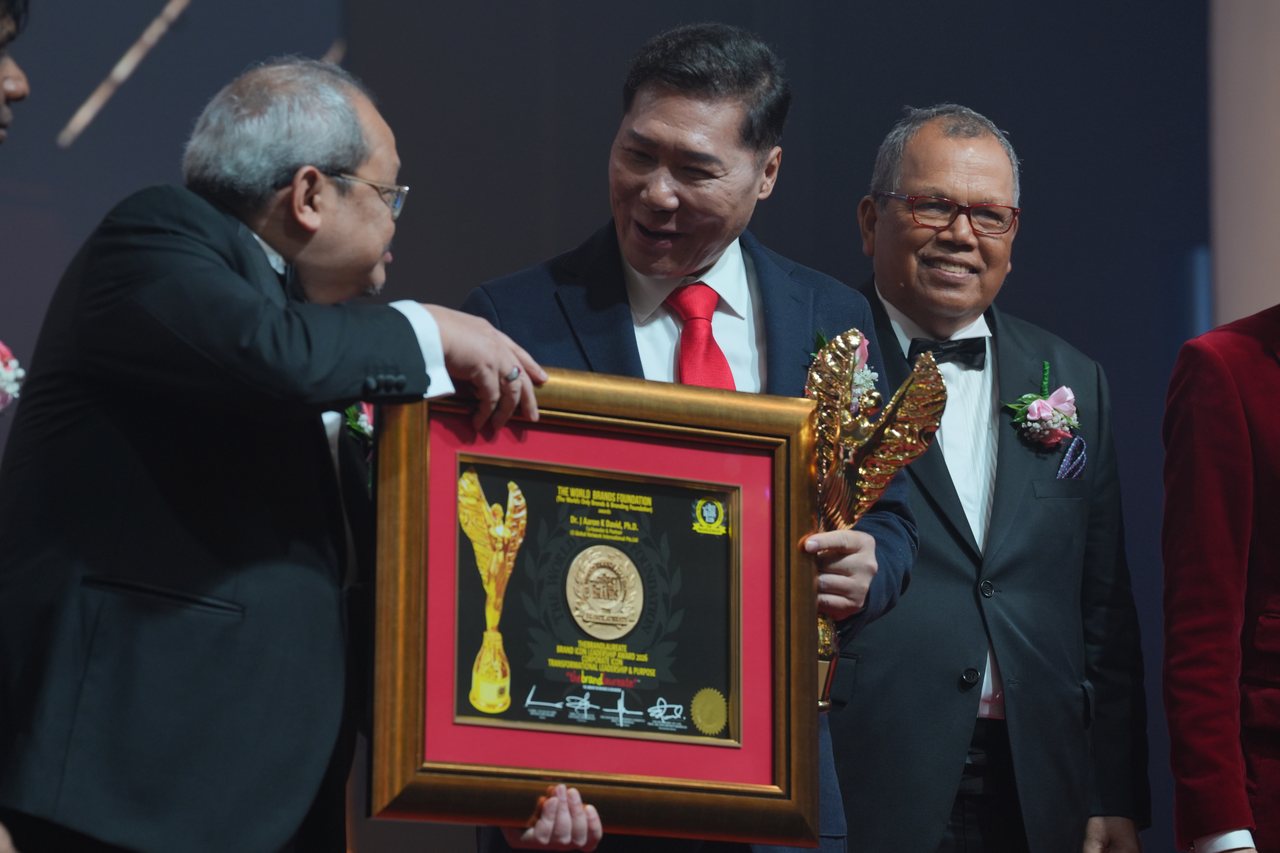 DR. J AARON K DAVID laughs as a presenter passes him the framed certificate, the gold trophy in his hand and Tun Md Raus Sharif smiling beside him