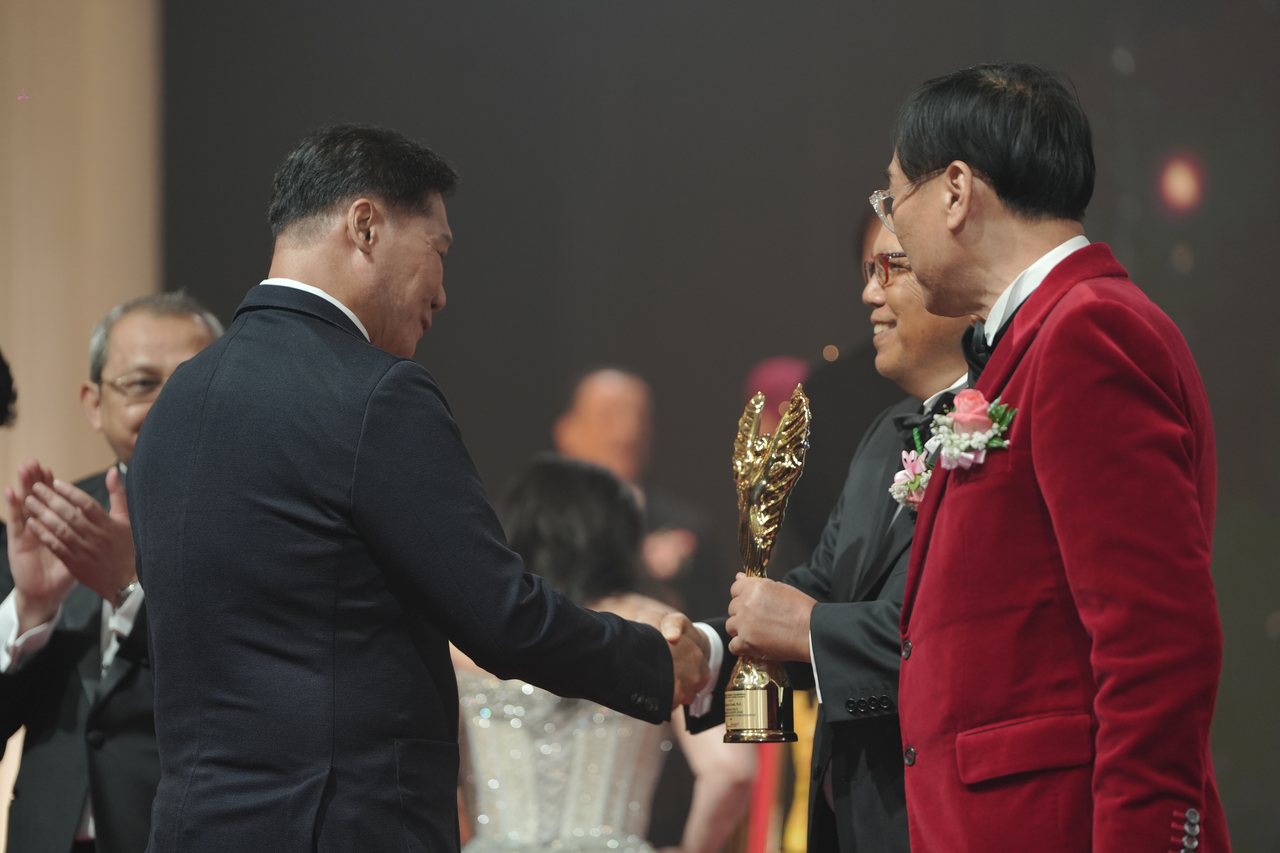 DR. J AARON K DAVID shakes hands with Tun Md Raus Sharif, who holds out the gold winged trophy to him, Prof. Dr. KKJohan in a red velvet dinner jacket beside them