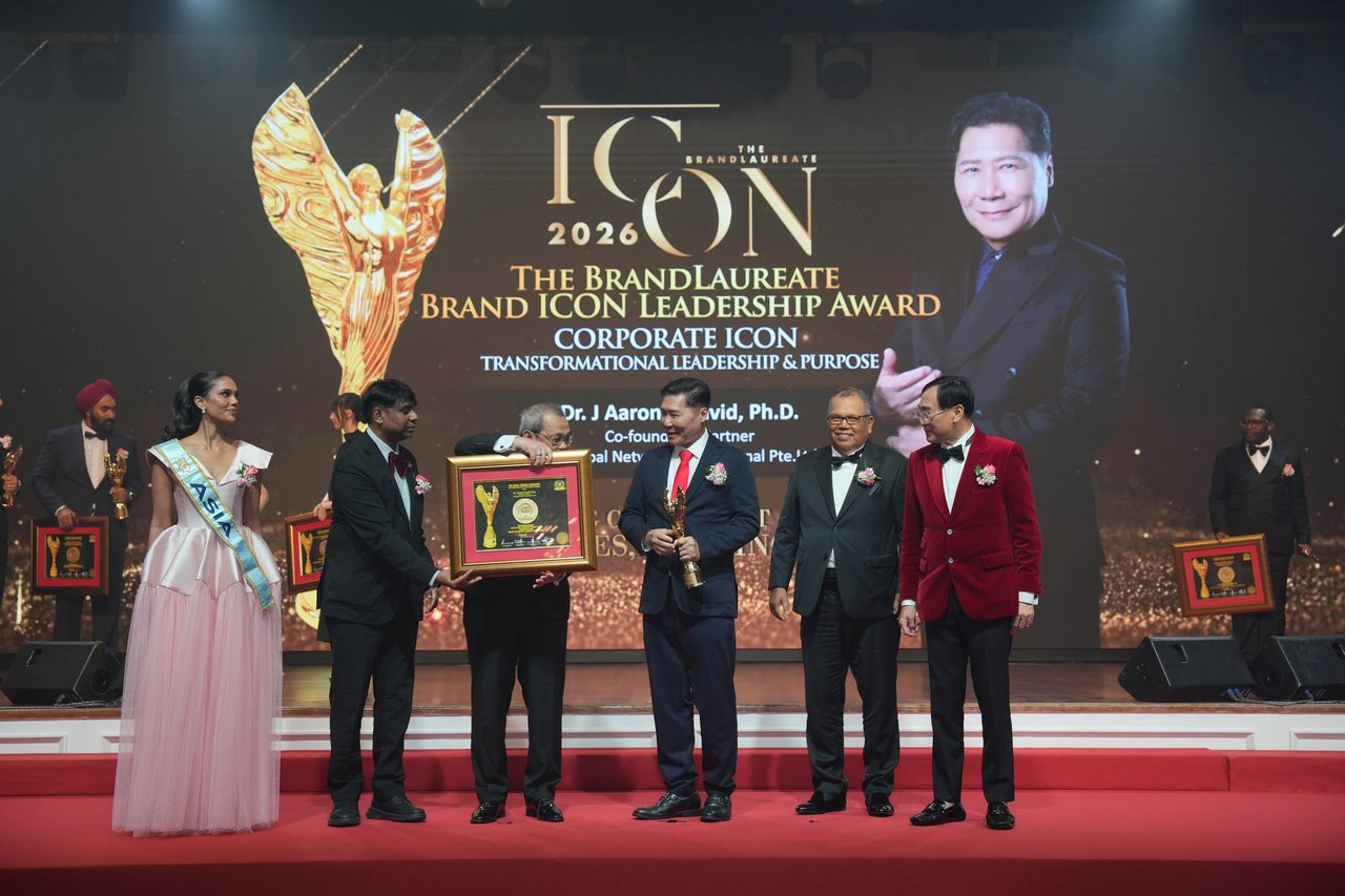 Left to right, Miss Universe Malaysia in a pale pink gown and sash, Prof. Dr. Edward Roy Krishnan and a presenter together handing over the framed certificate, DR. J AARON K DAVID in a red tie holding the gold trophy, Tun Md Raus Sharif standing beside him and Prof. Dr. KKJohan in a red velvet jacket, beneath the screen showing The BrandLaureate Brand ICON Leadership Award, Corporate Icon, with his name and portrait.