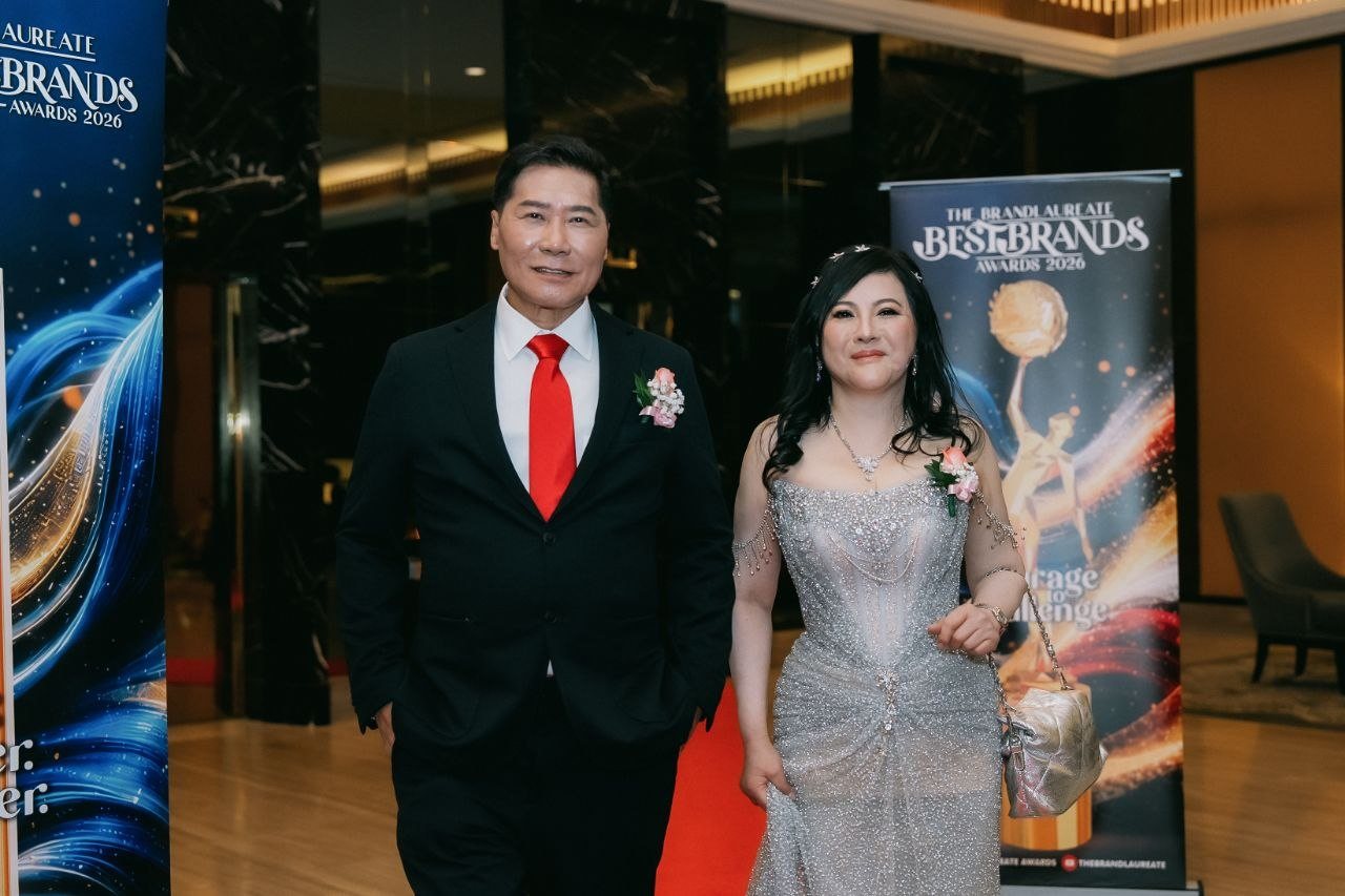 DR. J AARON K DAVID and DR. SHEKINAIH SIEW SIN YAP stand on the red carpet in the lobby beside the tall banner of The BrandLaureate BestBrands Awards 2026
