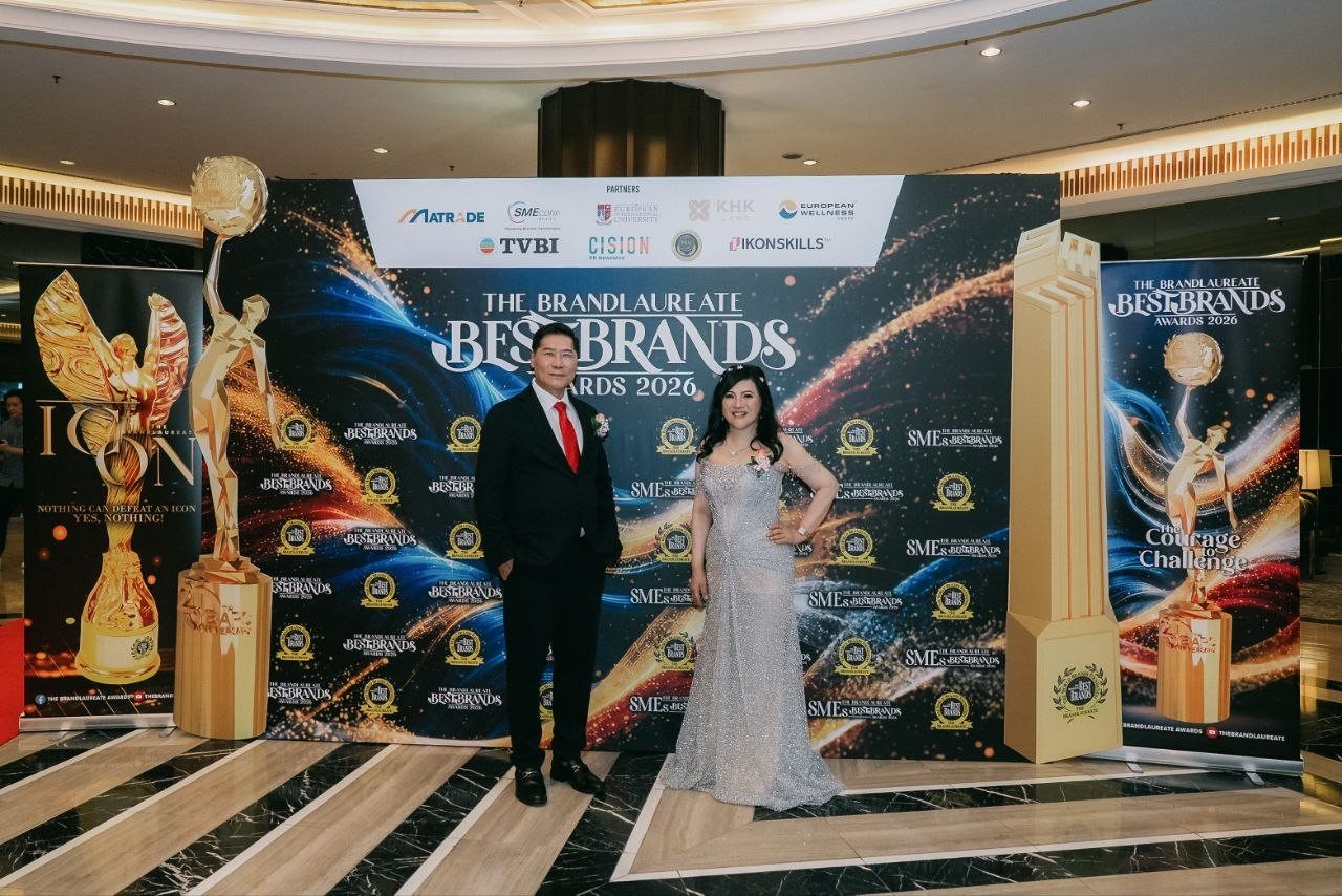 DR. SHEKINAIH SIEW SIN YAP and DR. J AARON K DAVID stand centred before The BrandLaureate BestBrands Awards 2026 backdrop in the domed lobby, with tall gold replicas of the tower and globe trophies at each side