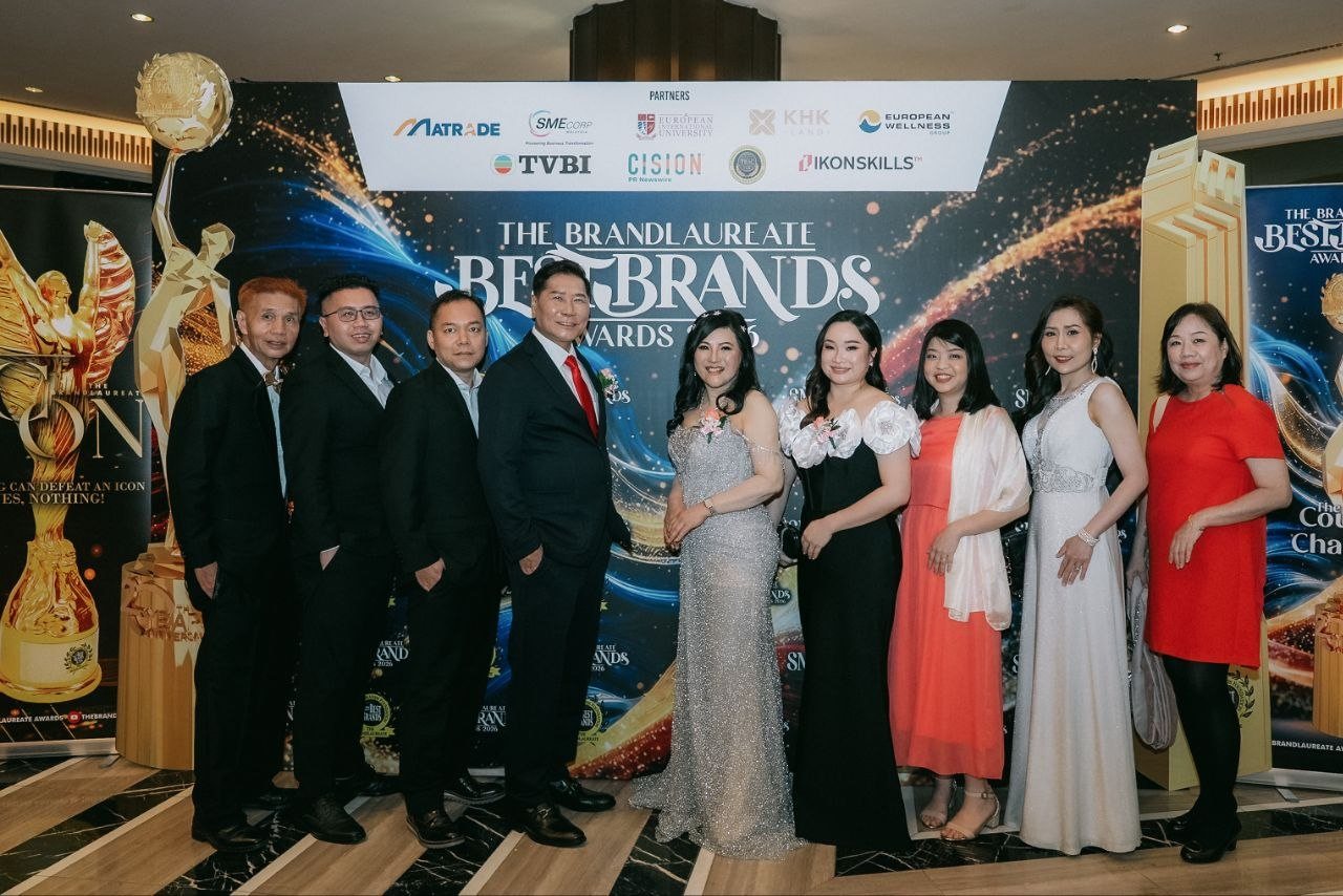 DR. J AARON K DAVID and DR. SHEKINAIH SIEW SIN YAP with Hilary Ng beside DR. SHEKINAIH SIEW SIN YAP and the team of CE Global Network International and Crowned Eagles Global in suits and evening gowns, before The BrandLaureate BestBrands Awards 2026 backdrop