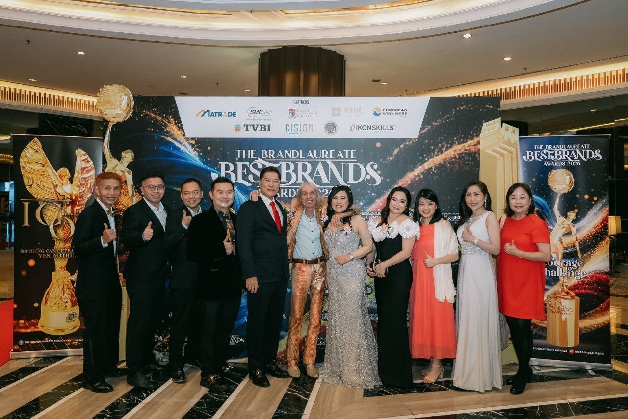 DR. J AARON K DAVID and DR. SHEKINAIH SIEW SIN YAP in a long row before The BrandLaureate BestBrands Awards 2026 backdrop with Alain Robert, in a gold jacket, Hilary Ng and the team of CE Global Network International and Crowned Eagles Global, several giving a thumbs-up