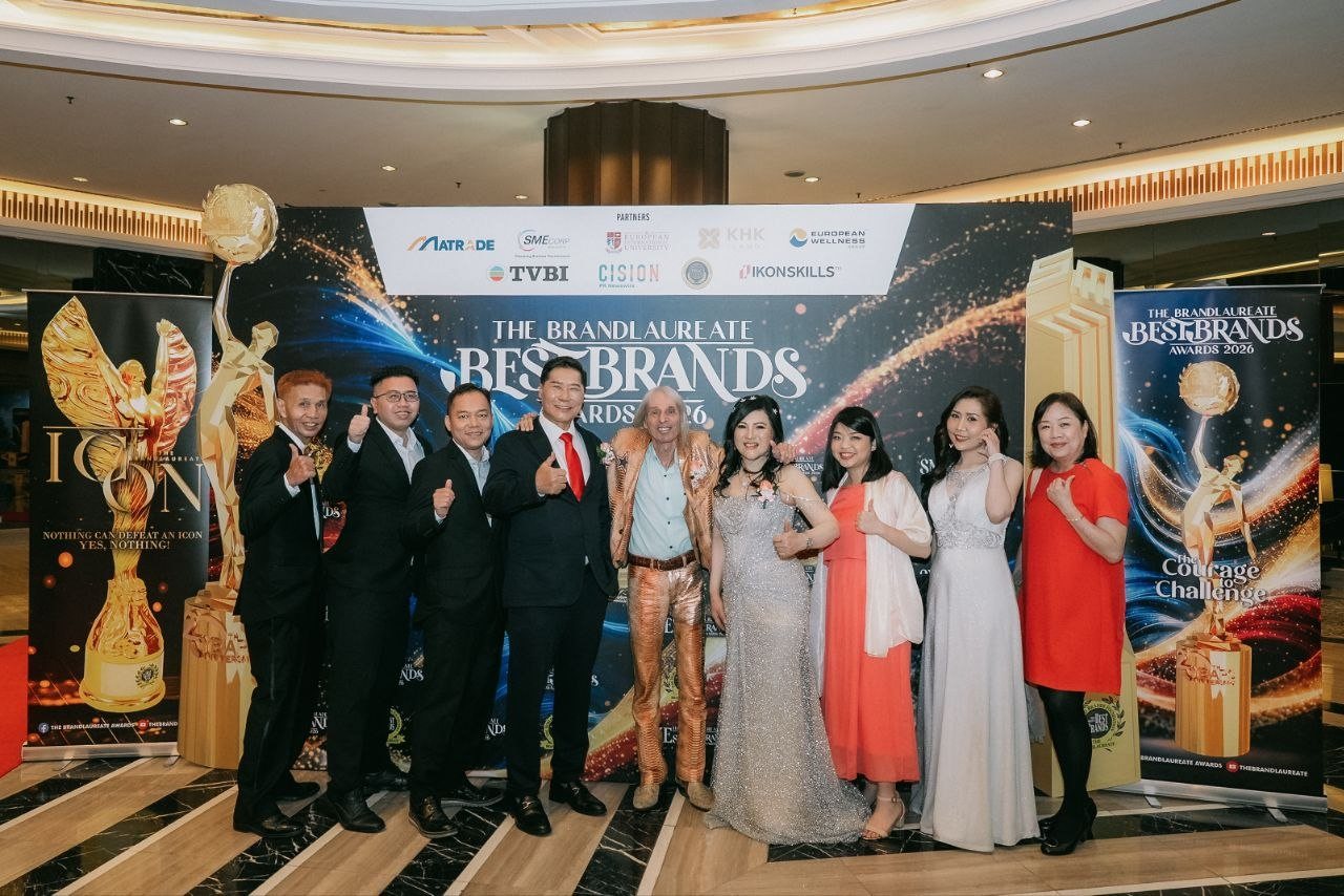 Before The BrandLaureate BestBrands Awards 2026 backdrop, three men in dark suits, DR. J AARON K DAVID, Alain Robert in gold, DR. SHEKINAIH SIEW SIN YAP, a guest in coral with a white shawl, Florence in an ivory sleeveless V-neck gown and a guest in red give a thumbs-up as the team of CE Global Network International and Crowned Eagles Global.