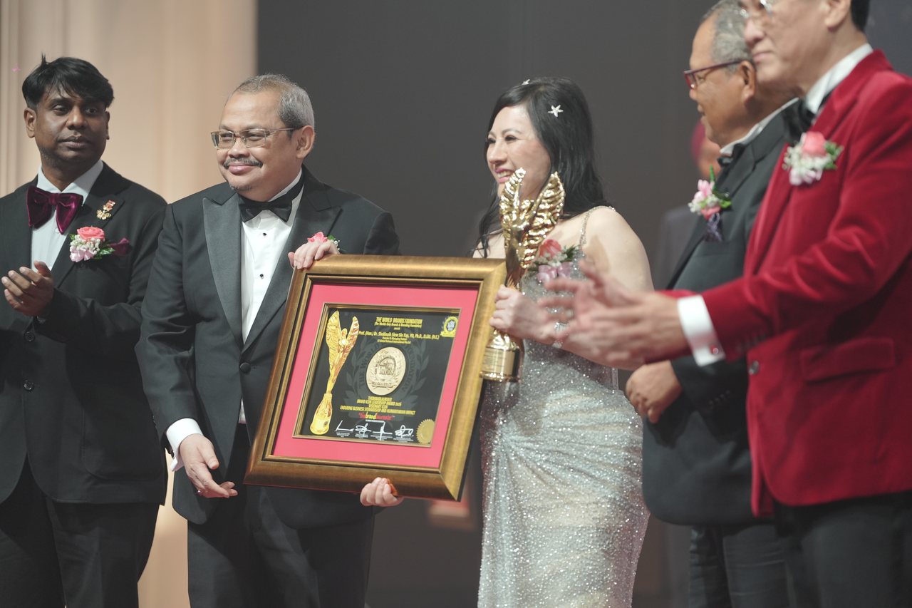 DR. SHEKINAIH SIEW SIN YAP holds the gold trophy as a presenter beside her holds up her framed certificate, Prof. Dr. Edward Roy Krishnan at the left and Prof. Dr. KKJohan applaud, and Tun Md Raus Sharif stands beside her