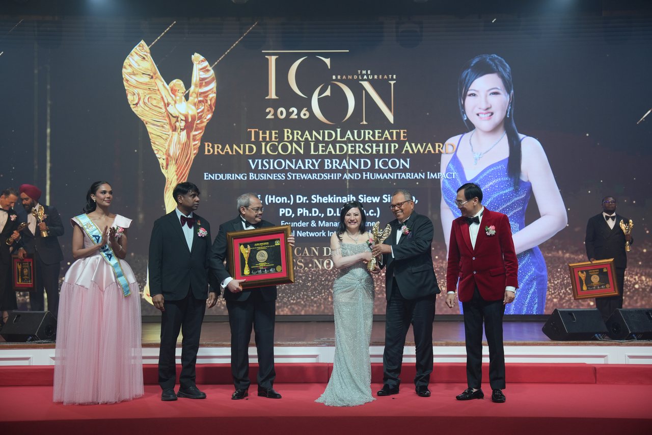 The full stage with DR. SHEKINAIH SIEW SIN YAP at the centre receiving her trophy from Tun Md Raus Sharif, Prof. Dr. Edward Roy Krishnan standing at left beside the certificate presenter, Prof. Dr. KKJohan at right and Miss Universe Malaysia applauding at far left, beneath the screen with her portrait and award title