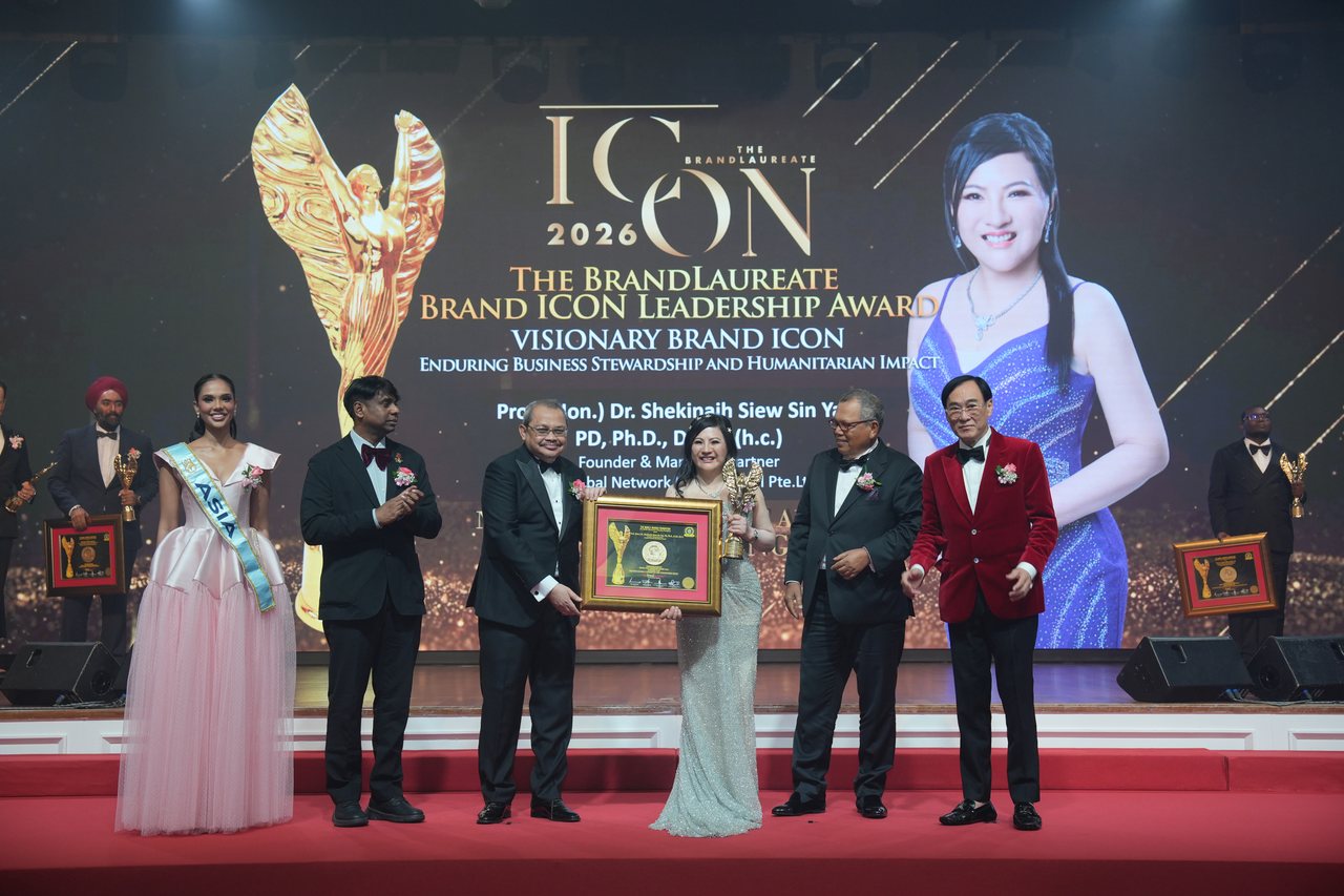 Left to right, Miss Universe Malaysia in a pale pink tulle gown and sash, Prof. Dr. Edward Roy Krishnan applauding, a presenter handing over the framed certificate, DR. SHEKINAIH SIEW SIN YAP in her silver beaded gown holding the gold trophy, Tun Md Raus Sharif, and Prof. Dr. KKJohan in a red velvet jacket, beneath the screen announcing The BrandLaureate Brand ICON Leadership Award, Visionary Brand ICON, Enduring Business Stewardship and Humanitarian Impact, with her portrait.