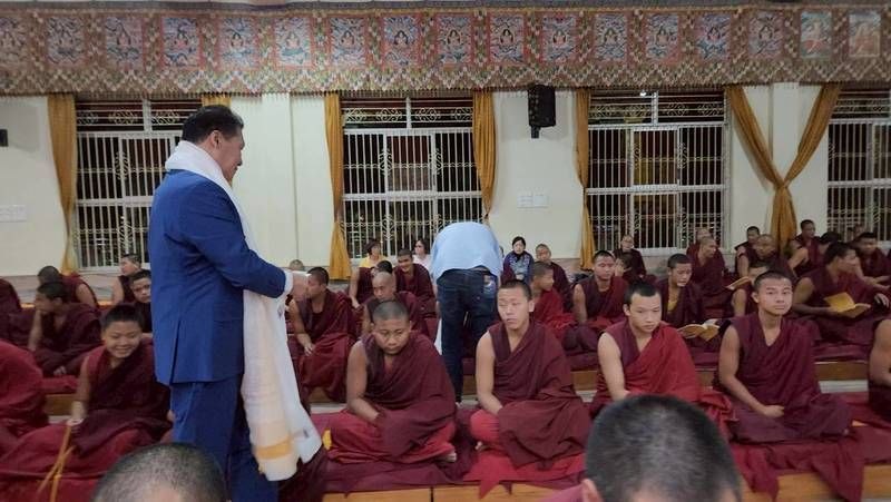 J AARON K DAVID walking with the white khata scarf among rows of young monks during the alms ceremony