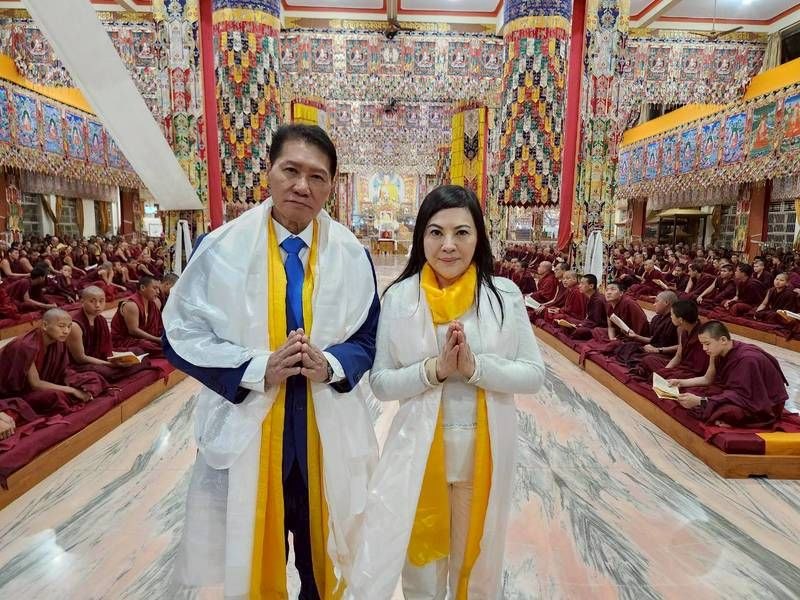 SHEKINAIH SIEW SIN YAP and J AARON K DAVID — formal portrait in the temple wearing the yellow khata, hundreds of monks seated on both sides
