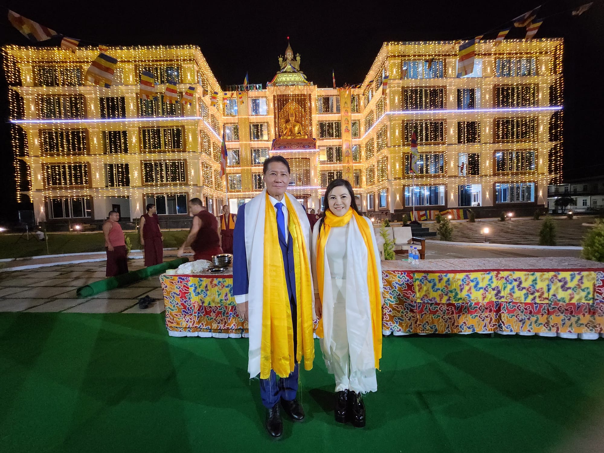 SHEKINAIH SIEW SIN YAP and J AARON K DAVID standing together before the illuminated golden temple façade at night, Doeguling Tibetan Settlement, Mundgod, January 2026