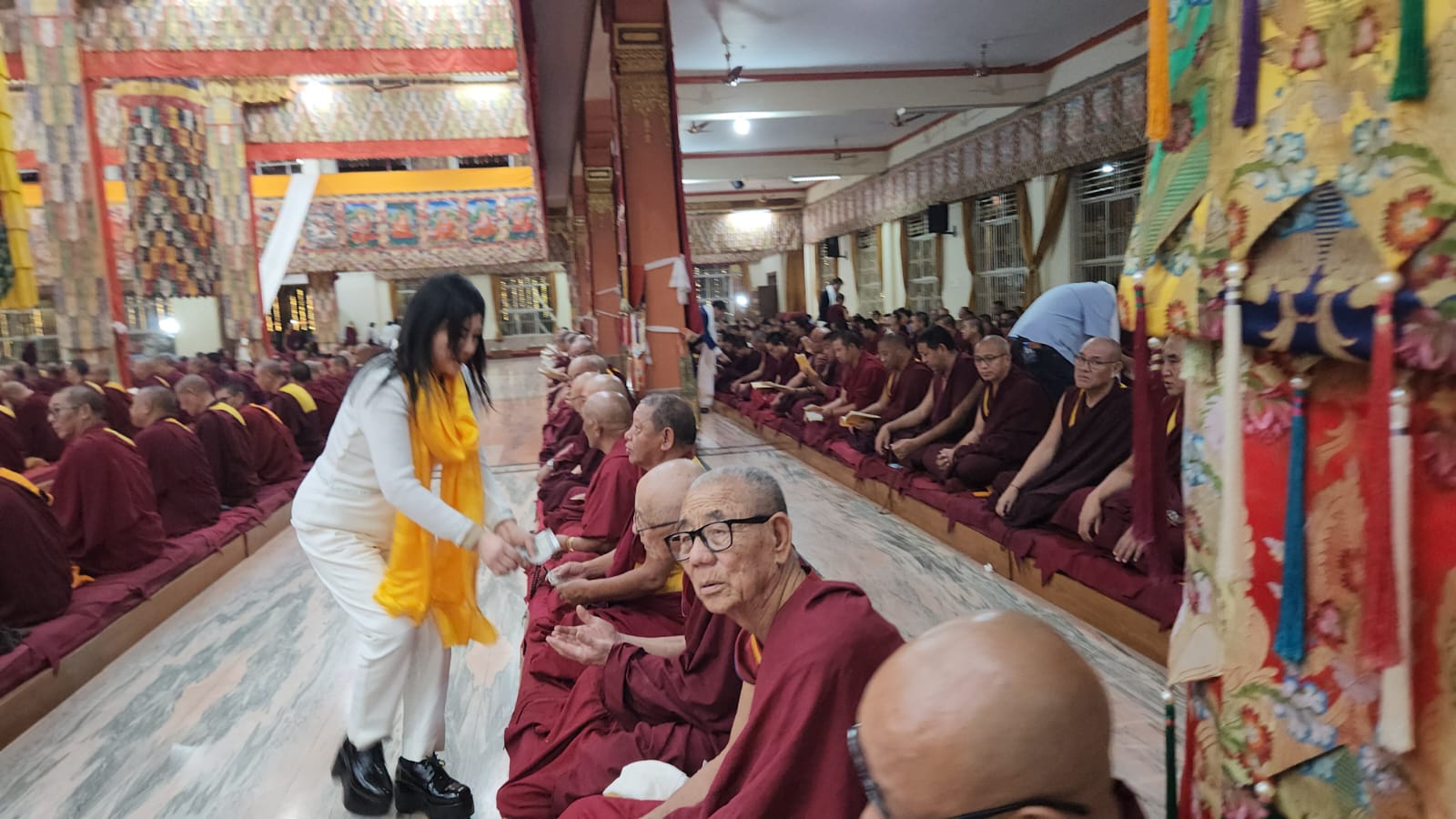 SHEKINAIH SIEW SIN YAP handing financial offerings to seated senior monks in the prayer hall, Doeguling, Mundgod, January 2026