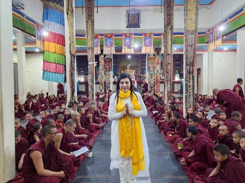 SHEKINAIH SIEW SIN YAP standing in the temple aisle with hundreds of young monks seated on either side, hands in prayer