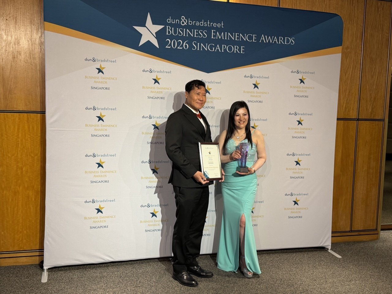 SHEKINAIH SIEW SIN YAP and J AARON K DAVID with the Business Eminence Awards 2026 certificate and trophy before the Dun & Bradstreet backdrop, Singapore