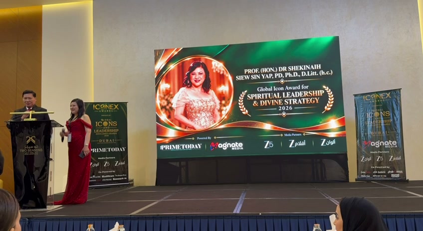SHEKINAIH SIEW SIN YAP on stage in Dubai beneath the screen announcing her Global Icon Award for Spiritual Leadership and Divine Strategy 2026