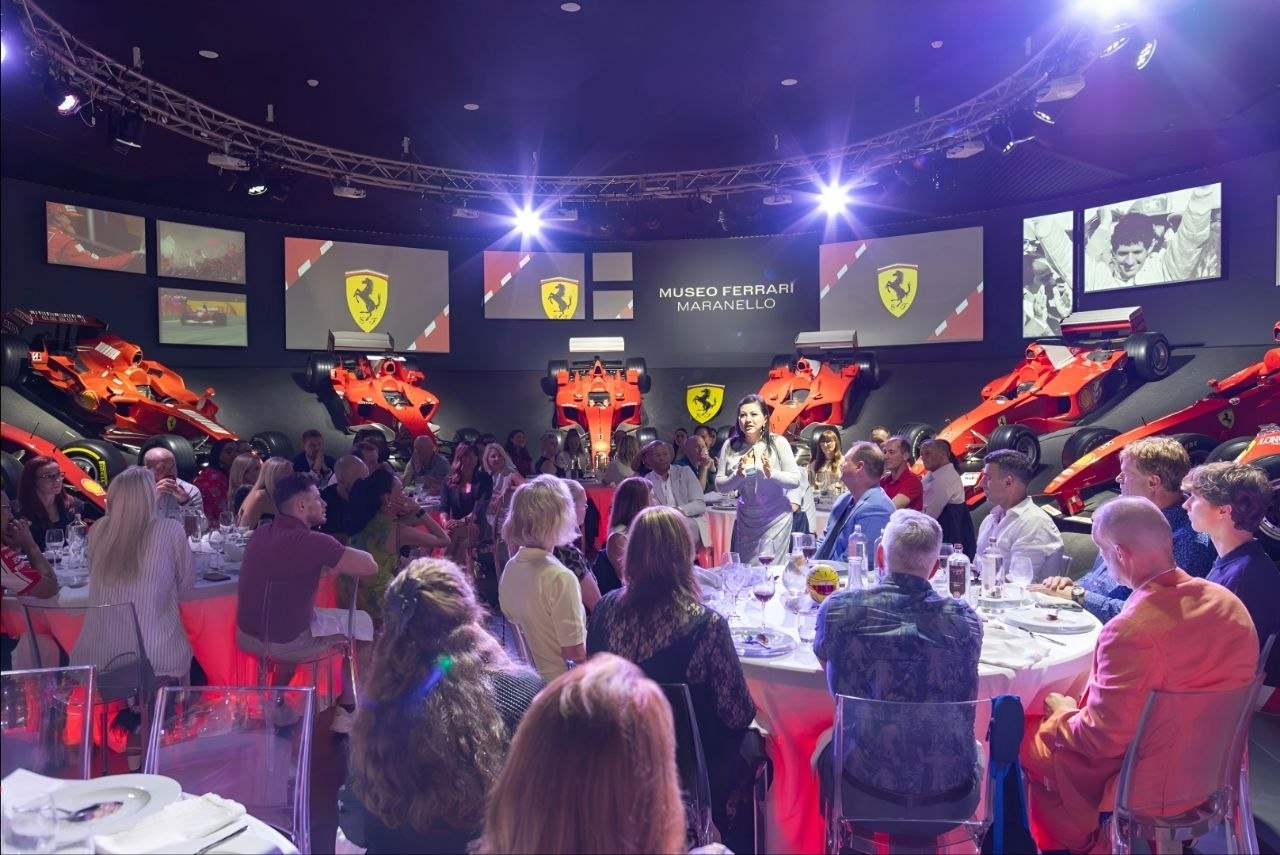 Guests at dinner inside Museo Ferrari, Maranello, beneath the museum's signage and Formula One cars