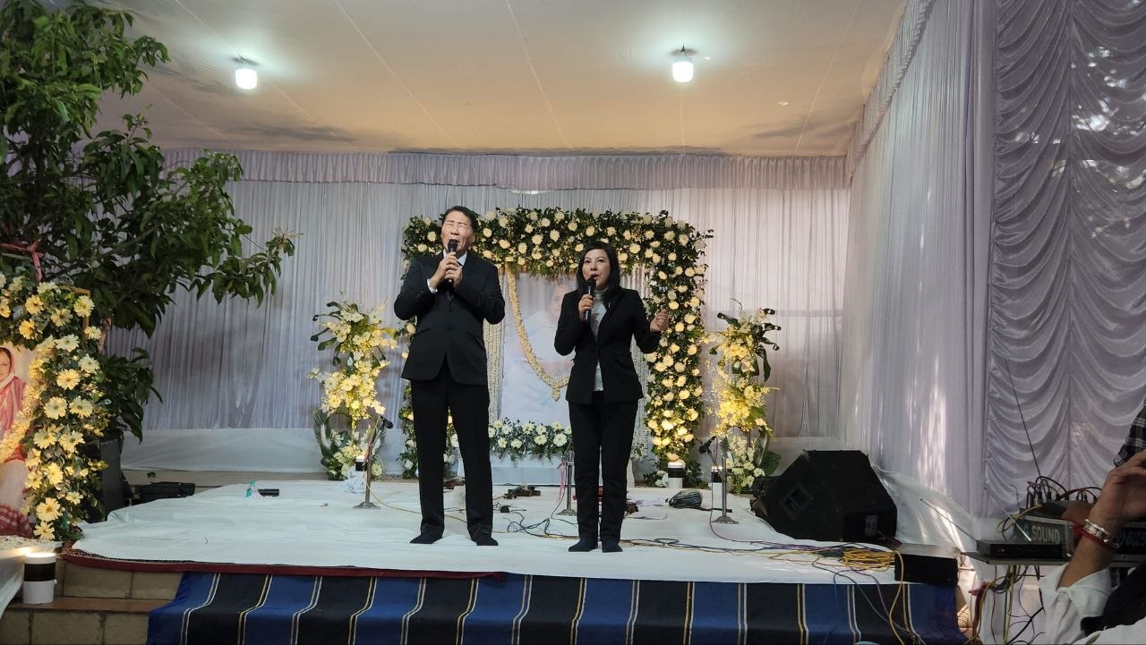 SHEKINAIH SIEW SIN YAP and J AARON K DAVID singing on the funeral service stage before the floral memorial, Sister Nivedita University, Kolkata