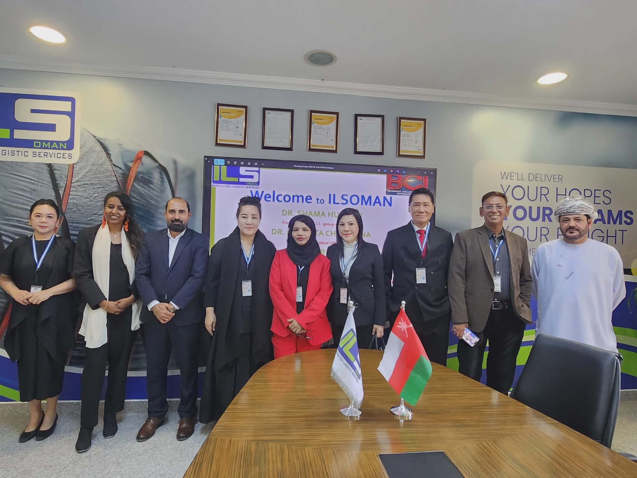 Delegation in the ILSOMAN conference room with the welcome screen, Sultanate of Oman flag, and ILSOMAN flag — SHEKINAIH SIEW SIN YAP and J AARON K DAVID among the honoured guests